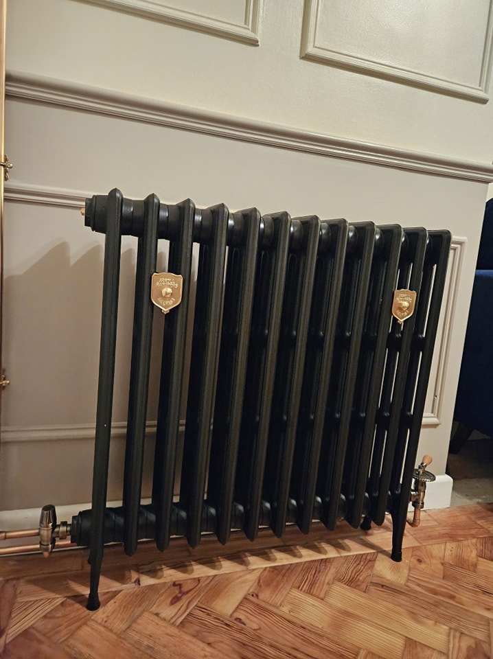 A black cast-iron column radiator with gold plaques on a herringbone floor