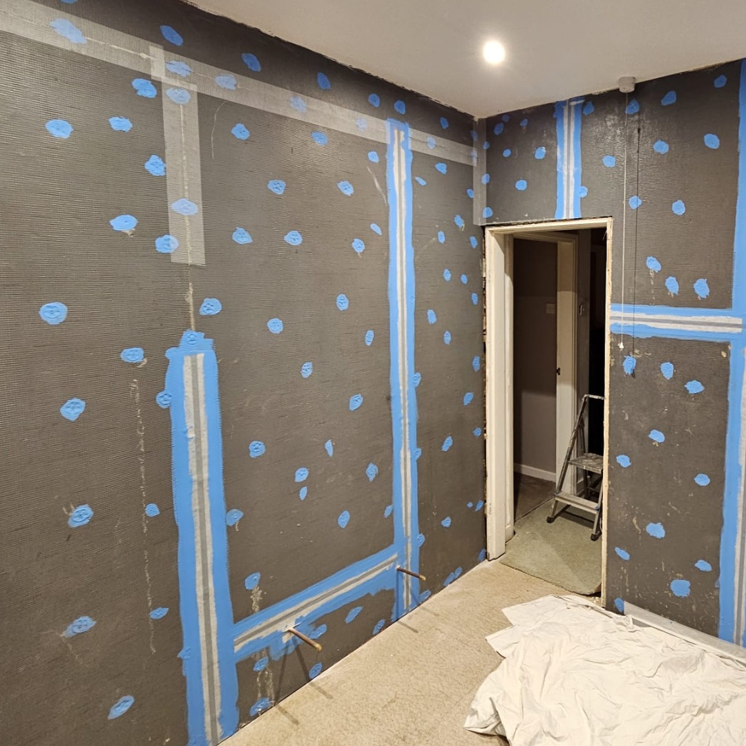 A bathroom stripped back to boarded walls with sealed and taped joints, ready for tiling