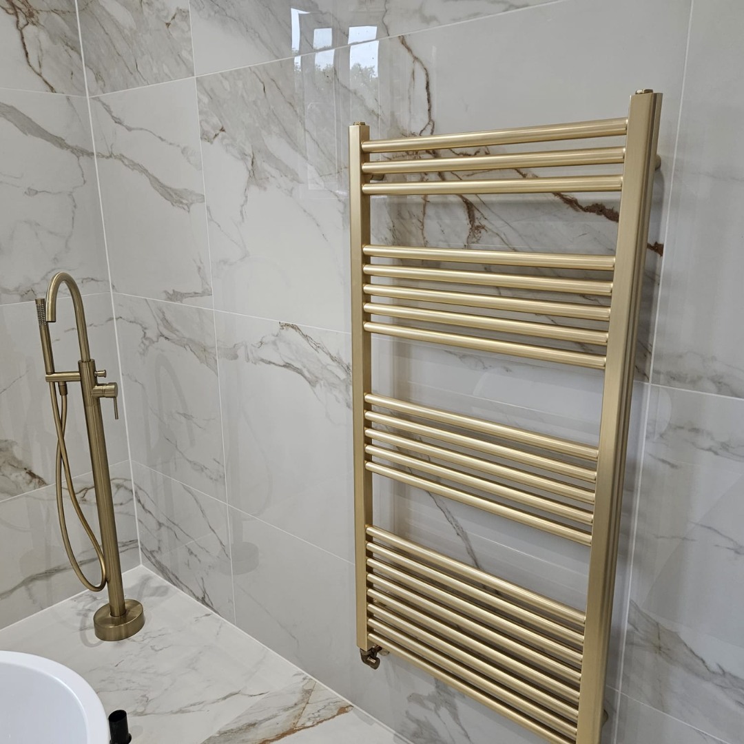 Brushed gold towel radiator and bath filler against marble-effect wall tiles