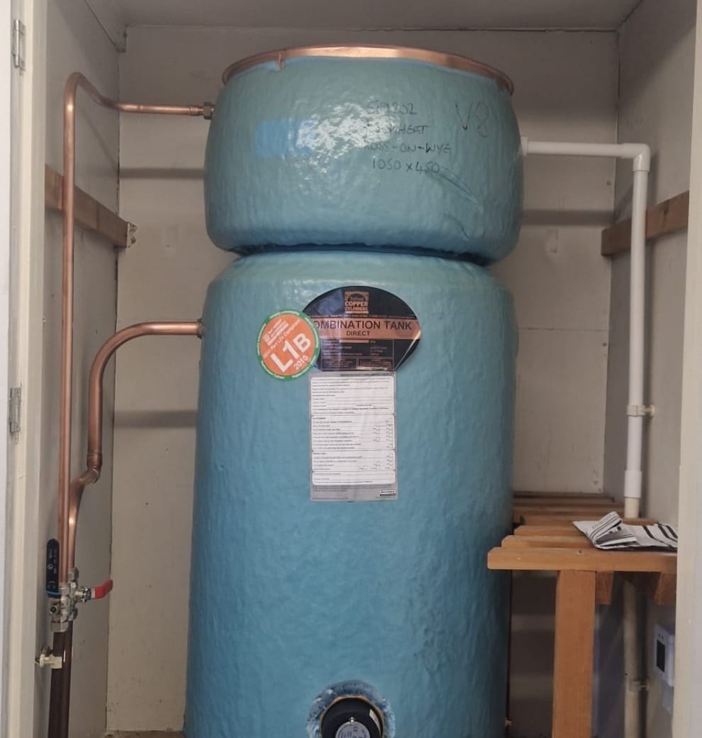 A copper hot water cylinder in an airing cupboard with copper pipework